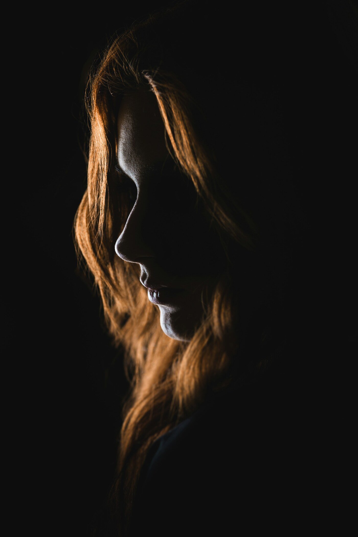 Mulher de perfil com a luz destacando o contorno do cabelo, em ambiente escuro